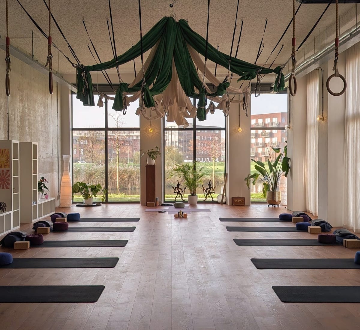 De studio van YogaStills in Purmerend: matten klaargelegd op de houten vloer, doeken aan het plafond en hoge ramen met uitzicht op het water
